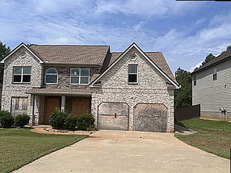 Two-story brick house before completion — boarded openings, bare lot, unfinished garage