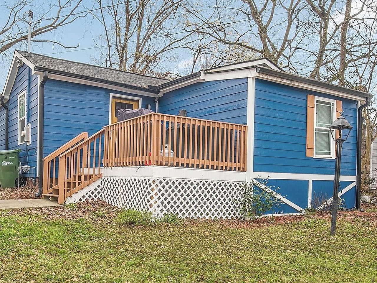 Bungalow after renovation — new blue siding, finished deck and rail, cleared lot