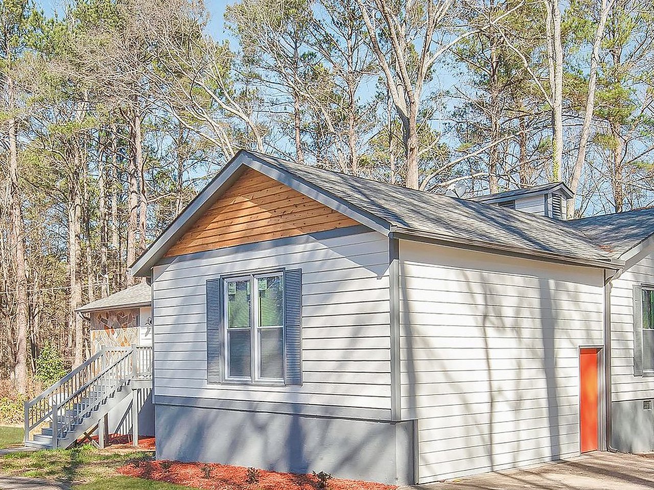 Cottage after renovation — new white siding, cedar gable, orange door, fresh landscaping